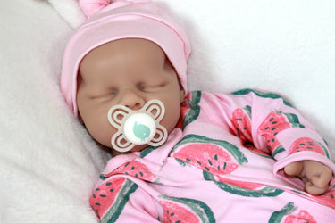 A baby doll holding a pacifier, dressed in a colorful outfit, with a gentle expression on its face.